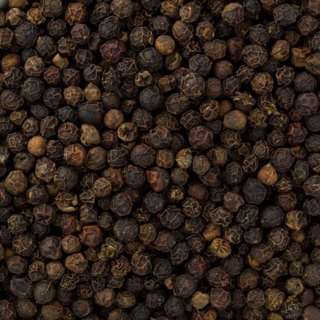 A close-up, top-down view of a dense pile of whole black peppercorns with wrinkled, dark brown to black skins.