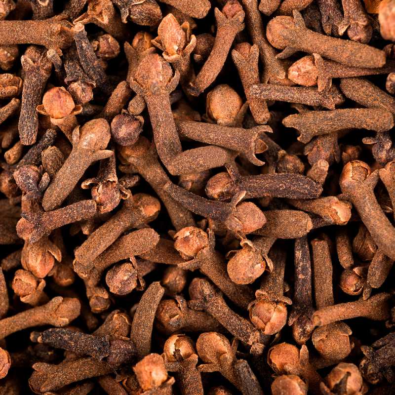 A close-up, top-down view of a dense pile of whole cloves, showing their characteristic brown stems and reddish-brown buds.