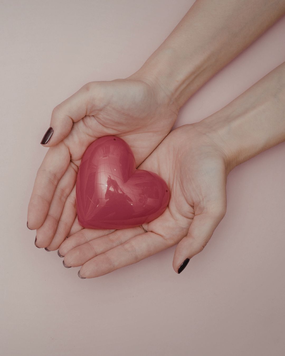 Two hands holding a pink heart-shaped object against a light background