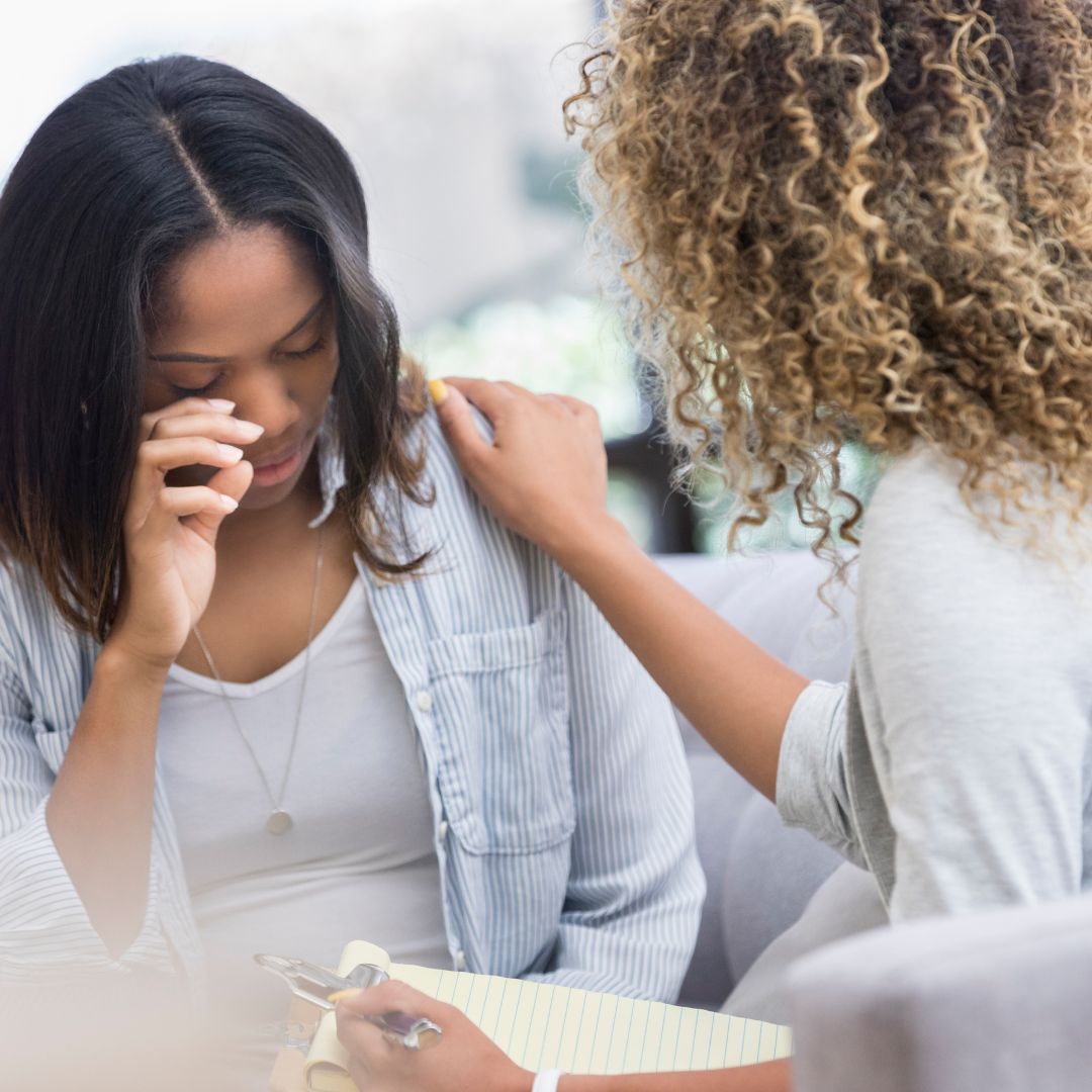 Two women in a therapy session, one holding her head in distress.