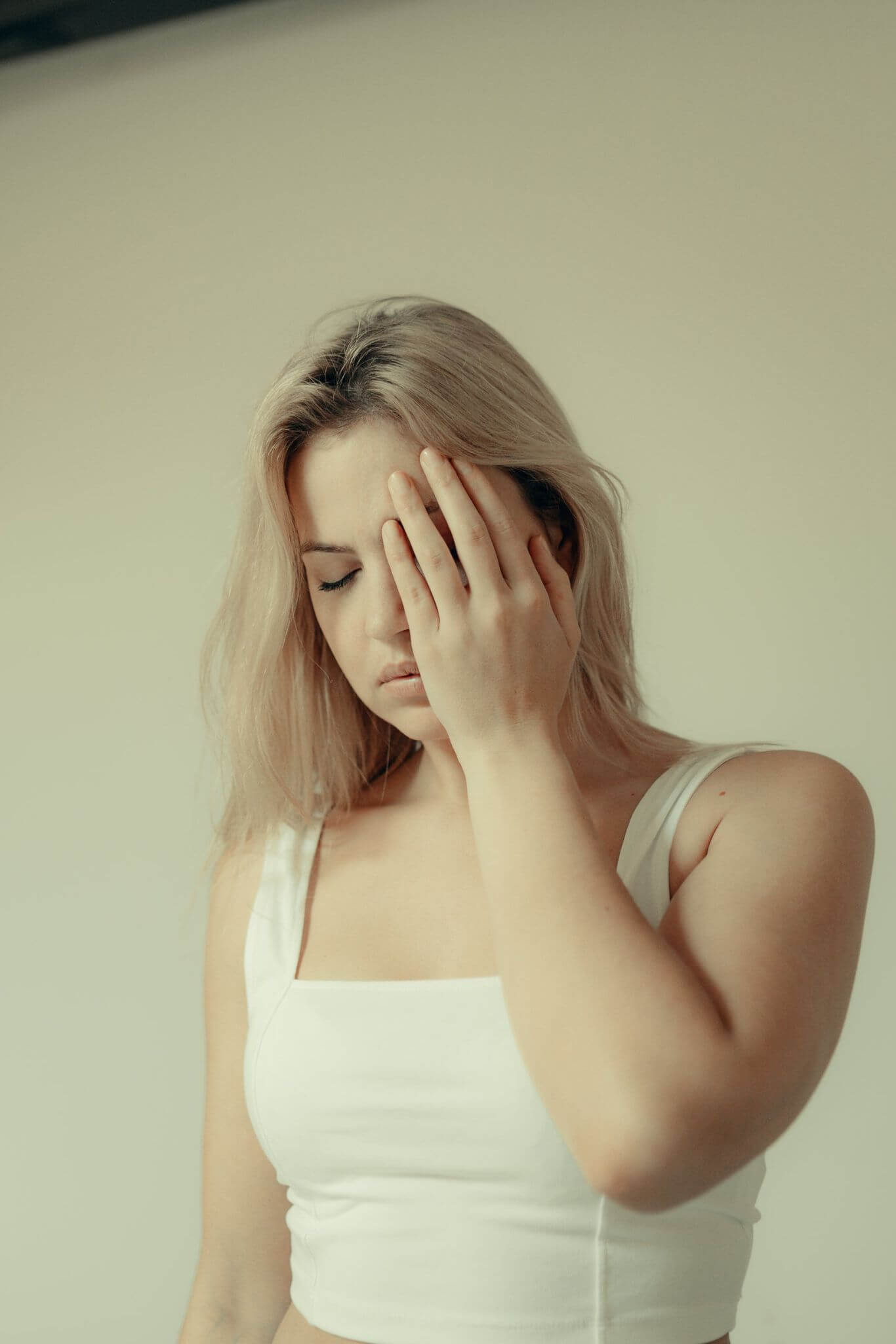 Woman in a white top with a neutral background, looking stressed out.